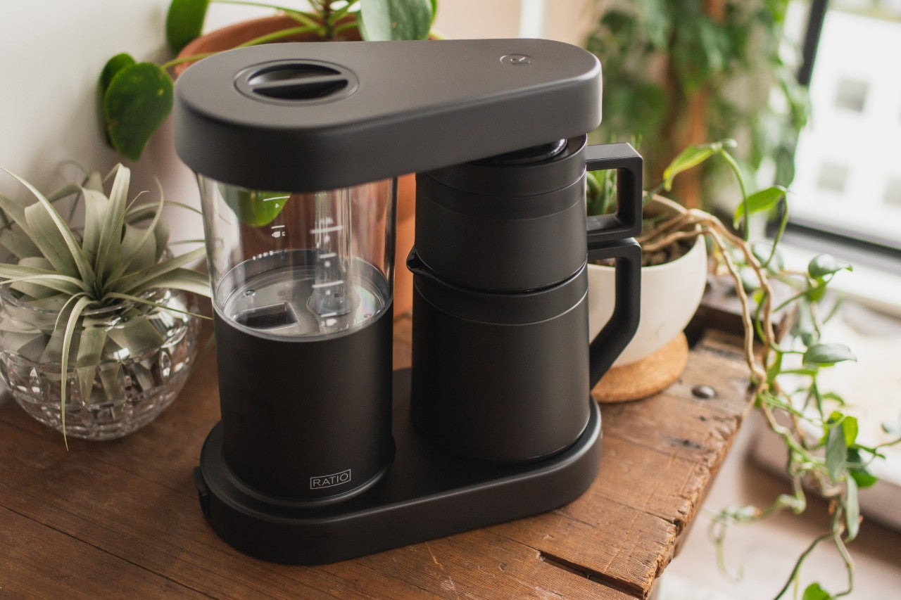 Ratio Six Coffee Maker sitting on a table surrounded by plants