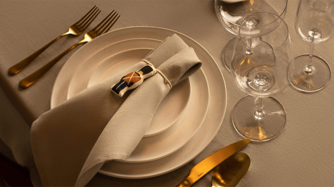 A ceramic dinnerware set with 3 different sized white plates, a napkin, gold cutlery, and wine glasses.